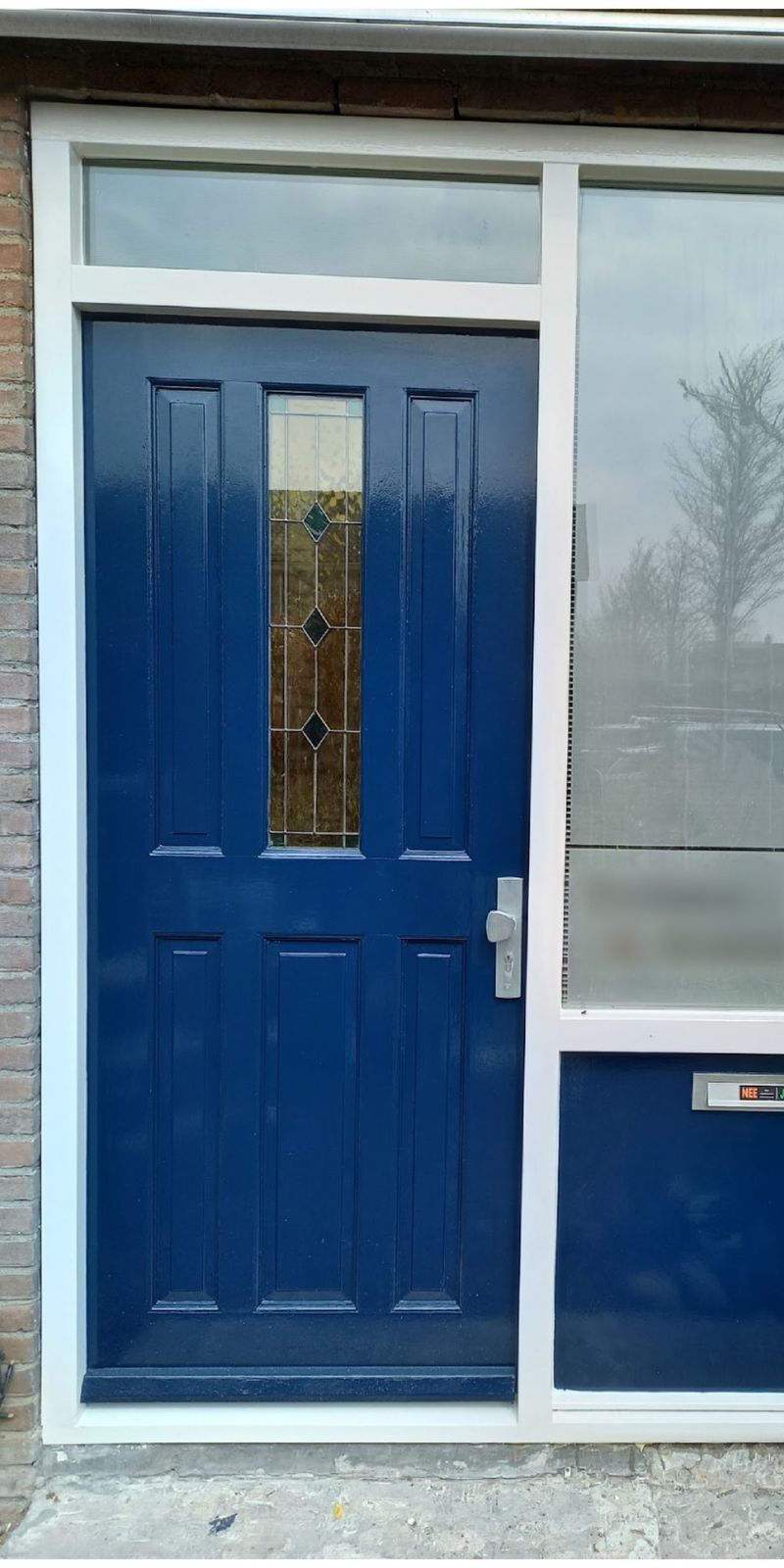 Dezelfde voordeur na het schilderwerk: glanzend diepblauw in een wit kozijn