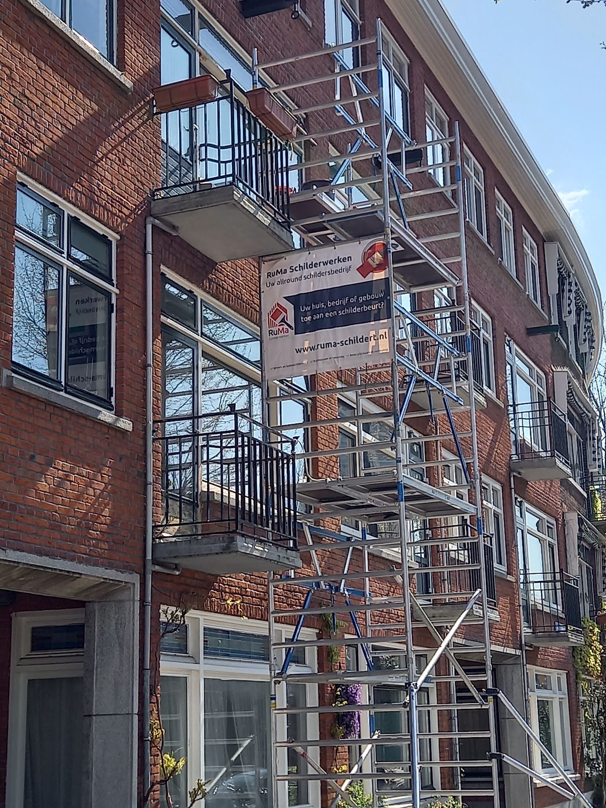 Spandoek van RuMa Schilderwerken aan een steiger voor een bakstenen flat: Uw allround schildersbedrijf