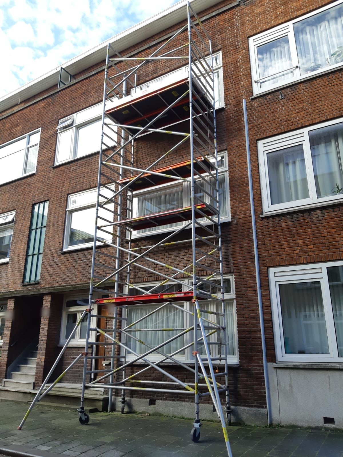 Rolsteiger tegen de bakstenen gevel van een portiekflat, waar RuMa aan het buitenschilderwerk werkt