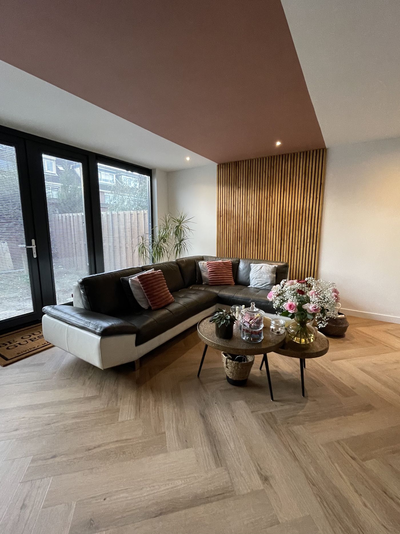 Woonkamer na het werk: houten lattenwand, verlaagd plafond in een warme donkere kleur en een visgraatvloer