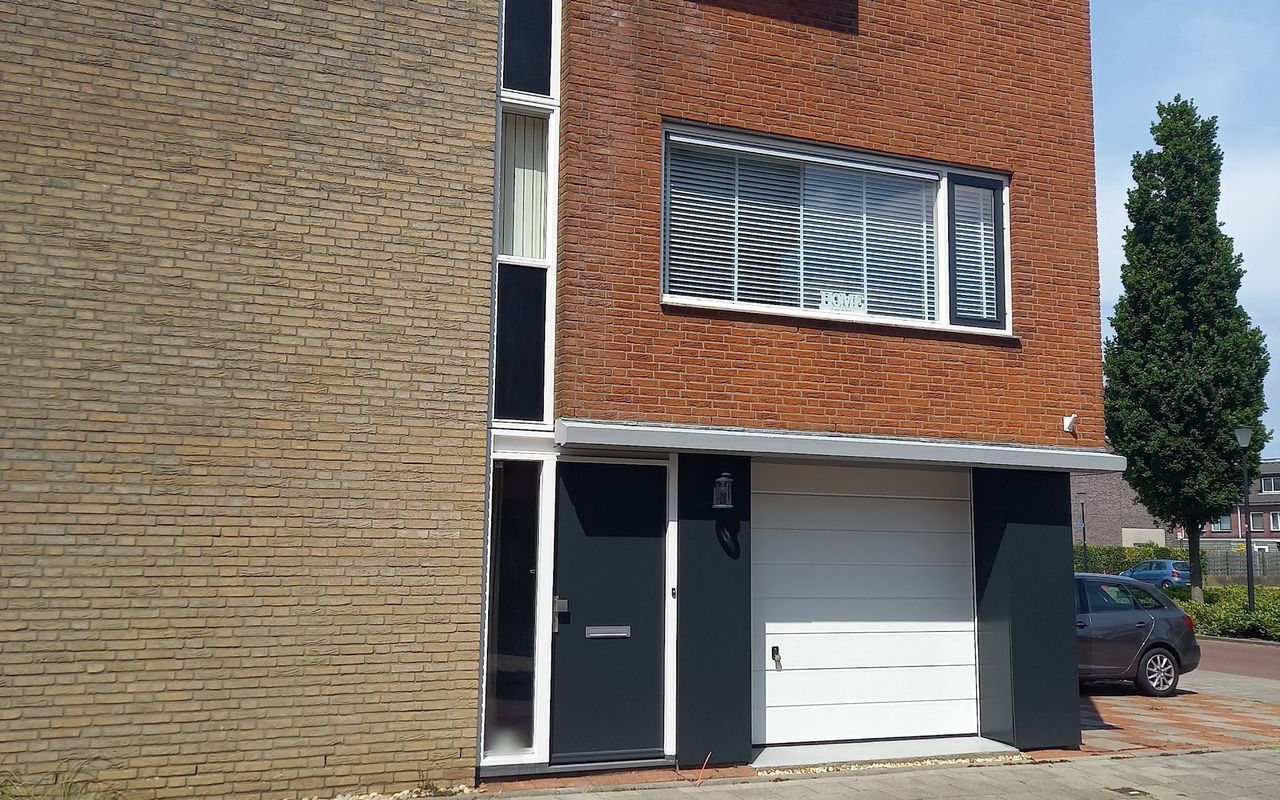 Hoekwoning van baksteen met antraciet geschilderde voordeur, kozijnen en zijpanelen en een witte garagedeur